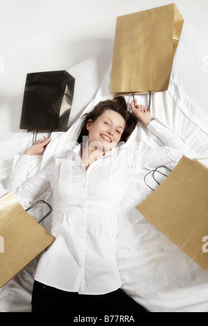 Young brunette woman lying happily in bed surrounded by shopping bags Stock Photo