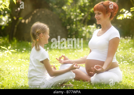 Girl and pregnant woman in yoga position in the garden Stock Photo