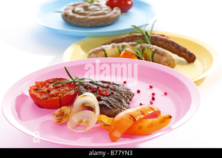 Grilled meat, sausages and vegetables on plates Stock Photo