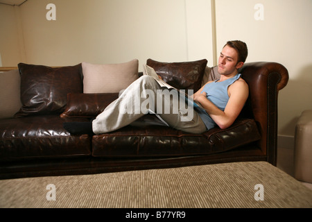 a portrait of a young good looking man relaxing, reading a newspaper whilst laying down on a leather sofa Stock Photo