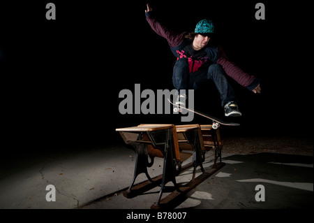 Skateboarder jumping over desks Stock Photo