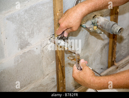 Plumbers hands using a wrench and pliers to loosen a pipe Closeup with room for text Authentic and accurate content depiction Stock Photo