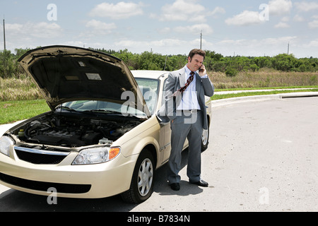 A businessman with a flat tire on the phone with the auto club Stock Photo