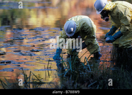 protective suited men collect water samples from polluted pond Stock Photo