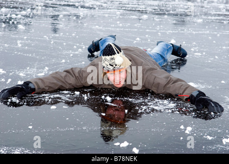 Young male (16-17) in winter clothes lying on frozen lake, smiling Stock Photo
