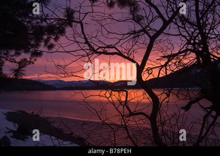 Pink alpenglow clouds at sunrise reflecting on ice on Donner Lake in California Stock Photo