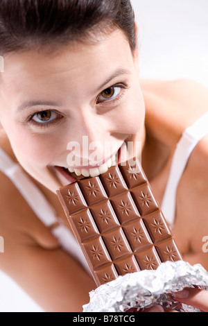 Young woman biting into chocolate bar, smiling Stock Photo