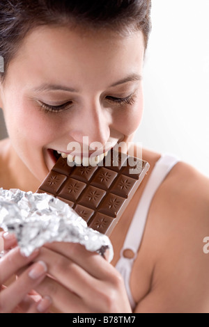 Young woman biting into chocolate bar, close up Stock Photo
