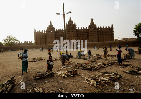 women arranging firewood in front largest mud brick or adobe building in the world, the Great Mosque of Djenné in Mali Stock Photo