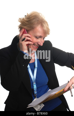 a busy female office worker with an id tag reviewing a file while speaking on a mobile phone Stock Photo