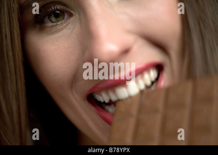 Young woman eating bar of chocolate, portrait, close-up Stock Photo