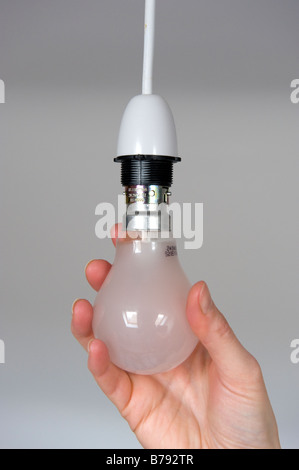 An old fashioned/traditional light bulb being plugged into a ceiling light socket. Stock Photo