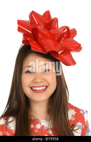 A young Asian woman smiles as she is wrapped in Christmas wrapping paper and topped with a big red bow Stock Photo