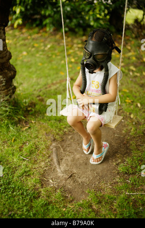 Five year old girl sits on swing wearing a gas mask Stock Photo