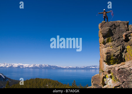 A mountaineer standing on top of a cliff above lake tahoe in Nevada coiling his climbing rope Stock Photo