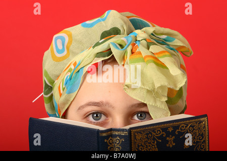 Teenage girl wearing hair curlers and head scarf looking old fashioned reading a book Stock Photo