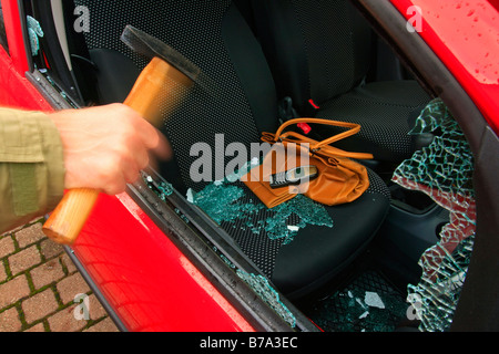 Car burglary, hand with hammer batters the side window, valuables left on the passenger seat, i.e. handbag, purse and mobile ph Stock Photo