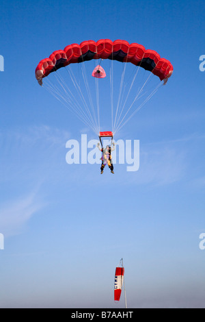 TANDEM PARACHUTING IN ENGLAND. TANDEM JUMPERS UNDER A RED PARACHUTE PREPARE FOR LANDING AS THEY PASS A LIMP WINDSOCK Stock Photo