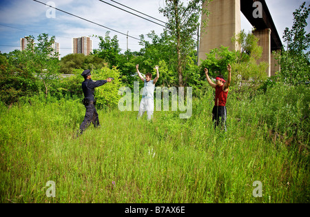Police Officer Arresting Two Men in a Grassy Field Stock Photo