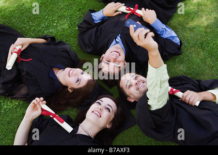 College Graduates Lying on Ground Reading Congratulatory text Message Stock Photo