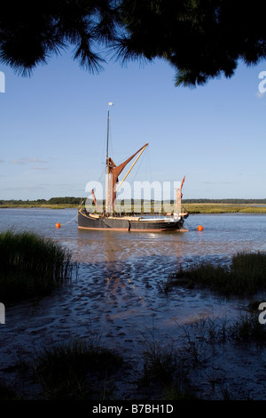 A Victorian spritsail barge lies at anchor in the lea of fir trees on the River Alde near Aldeburgh Stock Photo