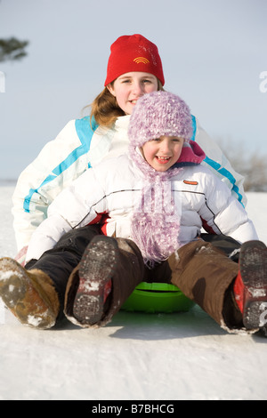 13 and 9 year olds slide down hill, Winnipeg, Canada Stock Photo