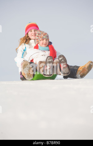 13 and 9 year olds slide down hill, Winnipeg, Canada Stock Photo