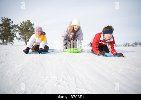 3 kids (14, 13 and 9 years old) sliding down hill, Winnipeg, Canada Stock Photo