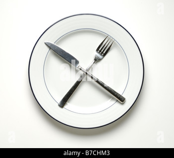 A round white dinner plate with a knife and fork crossed. Stock Photo