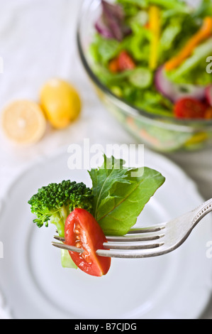 various lettuce leaves tomato and brocolli on fork with wine plate and salad bowl in background Stock Photo