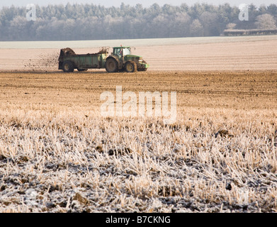 A tractor muck spreading in a frost covered field Stock Photo