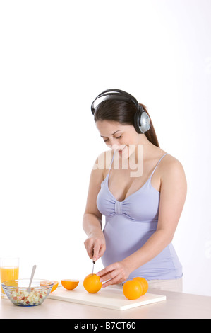 Pregnant young woman wearing headphones cutting oranges