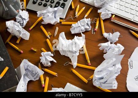 An office desk cluttered with pencils and crumpled paper Stock Photo