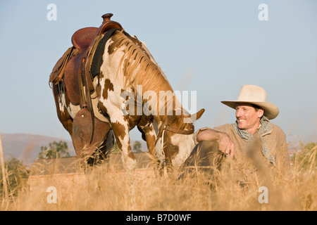 A cowboy sitting in long grass with his horse Stock Photo