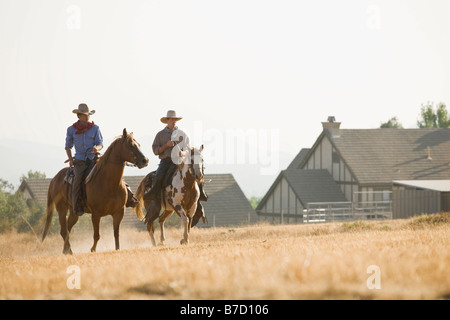 Two cowboys riding horses through a field Stock Photo