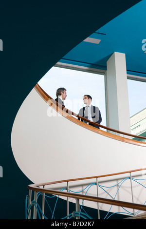 Two businessmen standing at the top of a staircase talking Stock Photo