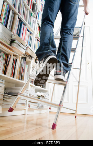 A man's legs climbing up a ladder that's about to tip over Stock Photo