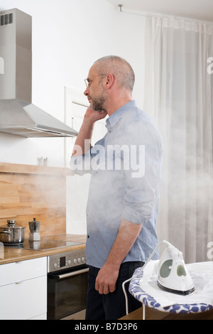 A man talking on the phone with his back to an iron which is burning his shirt Stock Photo