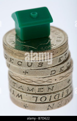 small toy house sitting on top of a stack of used pound coins on a white background Stock Photo