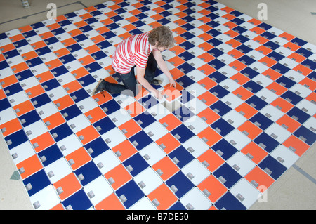 A young man putting the last set of bathroom scales into an artwork he has designed using household objects Stock Photo