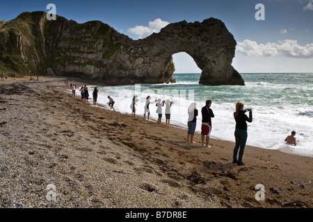 Young visitors admire the view and enjoy the surf on a summers day at Durdle Door on the Dorset coast Stock Photo