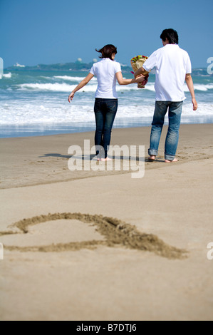 Young couple walking on the beach and holding a bunch of flowers Stock Photo