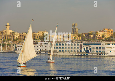Traditional wooden sailing boats or Feluccas sailing on the river Nile with Nile cruise boats moored at Luxor Egypt Middle East Stock Photo