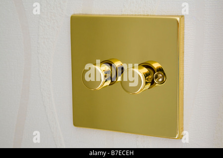 Gold metal double electric dimmer light switch on a wall. England UK Britain Stock Photo