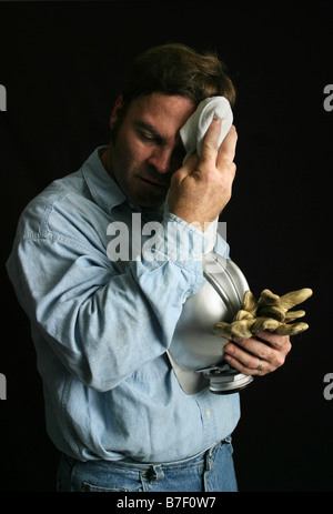 A tired coal miner wiping dirt and sweat off his brow dramatic side light to simulate being in a mineshaft Stock Photo