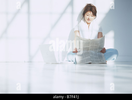 Woman reading newspaper on floor Stock Photo
