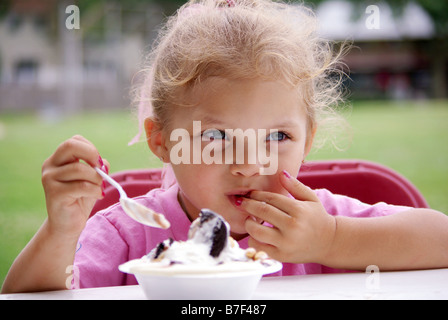A biracial four year old girl eats a bowl of ice cream at a picnic. Stock Photo