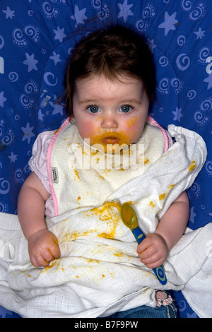 A baby girl holds a spoon during feeding Stock Photo