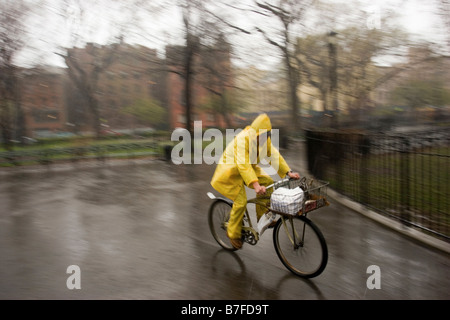 food delivery person riding a bicycle in the rain wearing a full yellow rainsuit.  images has motion blur Stock Photo