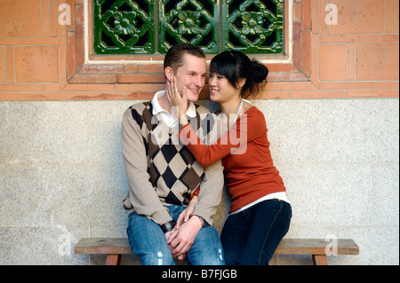 Young Couple Sitting On Bench Holding Each Other In Traditional Chinese Park, Taiwan Stock Photo